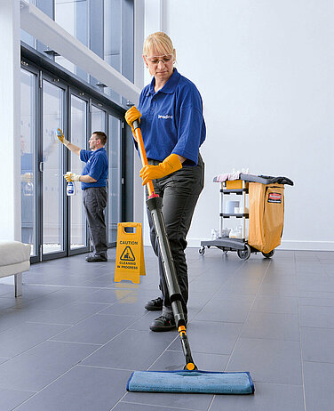 A Leadec employee cleaning the floor of a foyer. 