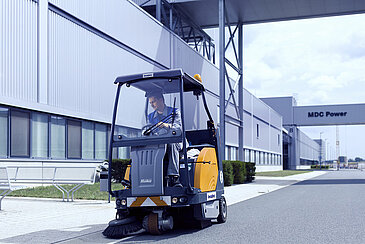 A Leadec employee cleaning the street with a sweeper at a factory site.