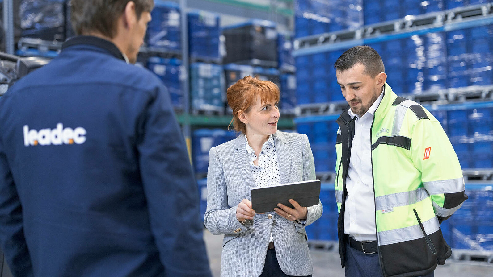 Leadec employees talking to a customer holding a tablet in a warehouse.